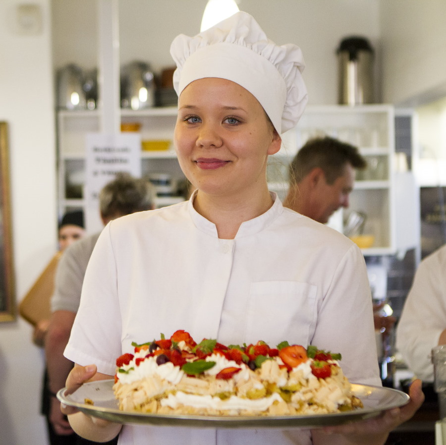 Hymyilevä kondiittori tuo tarjolle kakkua, jossa mansikoita, marenkia ja kermavaahtoa.