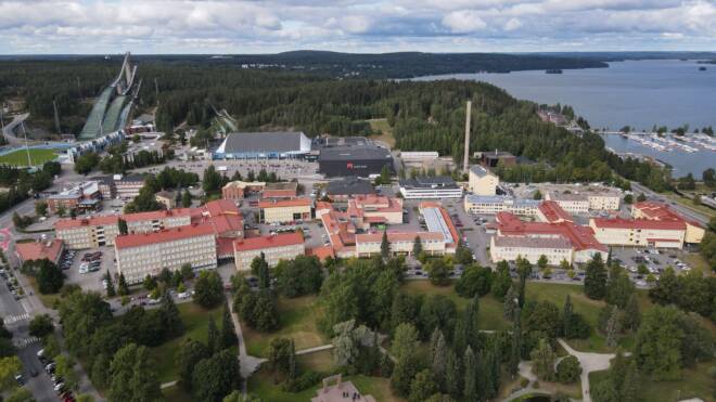 Ilmakuva Salpauksen Lahden keskustakampukselta, jossa on punakattoisia rakennuksia vehreyden ympäröimänä. Vasemmalla on hyppyrimäki ja oikealla suuri järvi laitureineen ja veneineen.