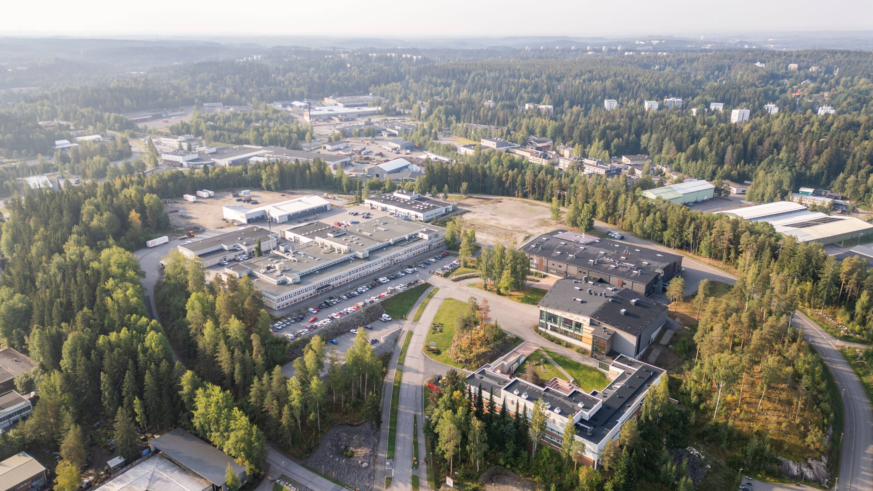 Ilmakuva Lahden Vipusenkadun kampukselta, jossa on useita rakennuksia tiheän metsän ympäröimänä. Tiet kiemurtelevat viheralueiden läpi ja pysäköityjä autoja näkyy rakennusten läheisyydessä.