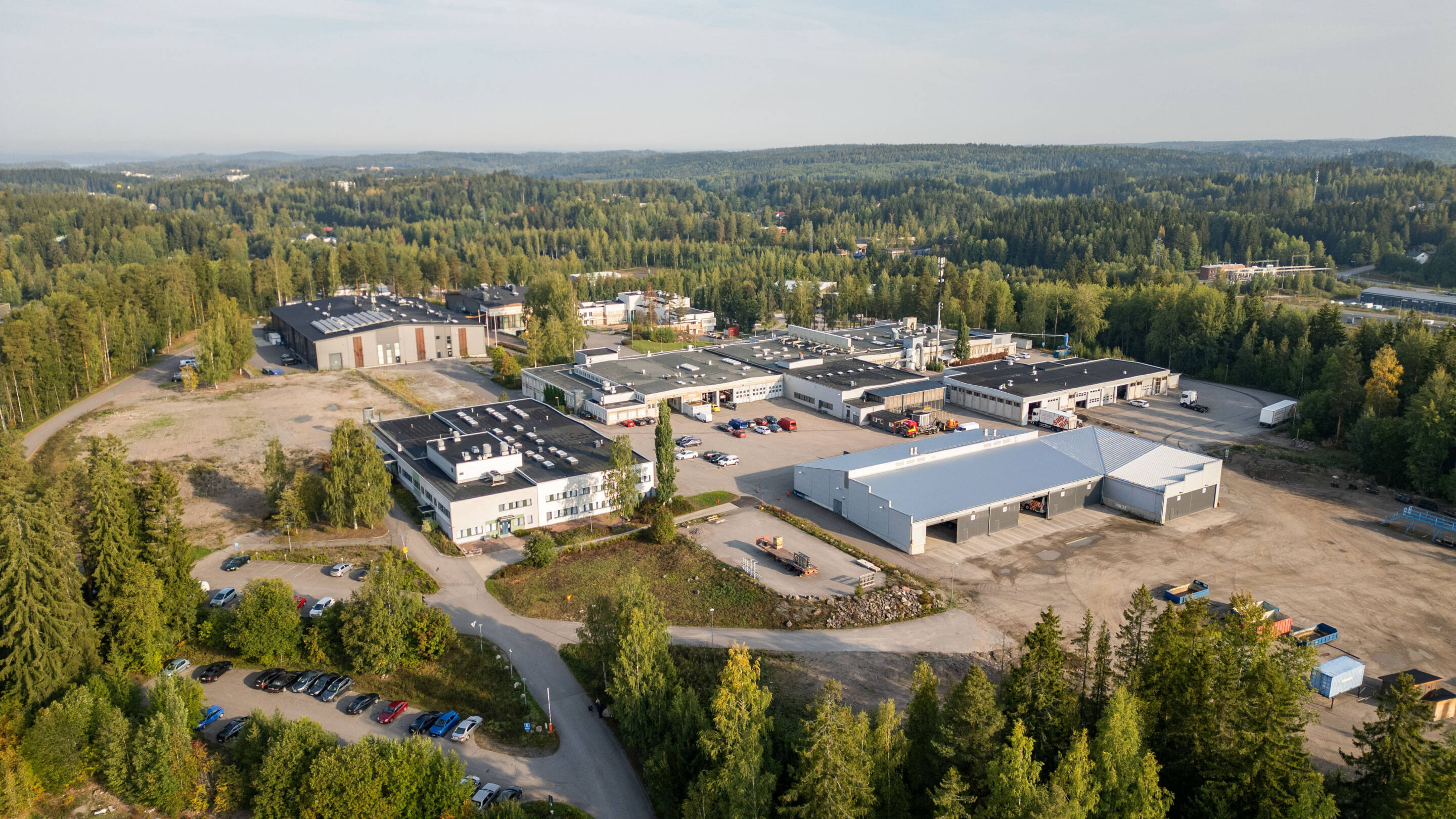 Ilmakuva Salpauksen Vipusenkadun kampuksesta, jota ympäröivät tiheät vihreät metsät. Näkyvissä on useita suuria rakennuksia ja varastoja, ja pysäköityjä ajoneuvoja. Tiet yhdistävät komplekseja, ja horisontissa näkyy puita.