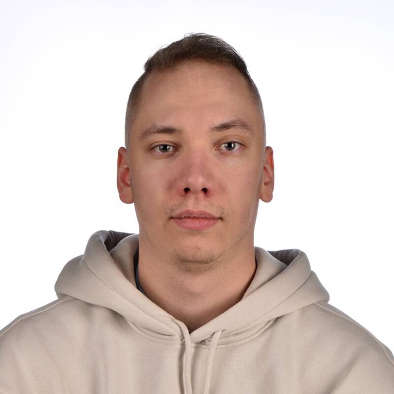 Nuori mies, jolla on lyhyet vaaleanruskeat hiukset ja vaaleat kasvotukka, ja yllään beige huppari, katsoo suoraan kameraan valkoista taustaa vasten.