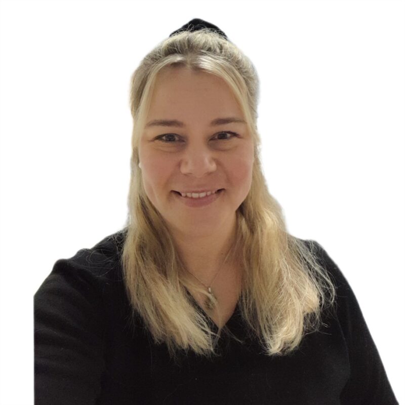 Pitkät vaaleat hiukset omaava henkilö hymyilee, yllään musta toppi ja hopeinen kaulakoru. he seisovat tavallista valkoista taustaa vasten.