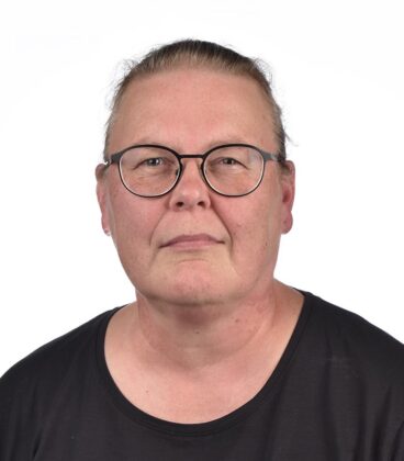 Henkilö, jolla on lasit ja musta paita valkoista taustaa vasten.