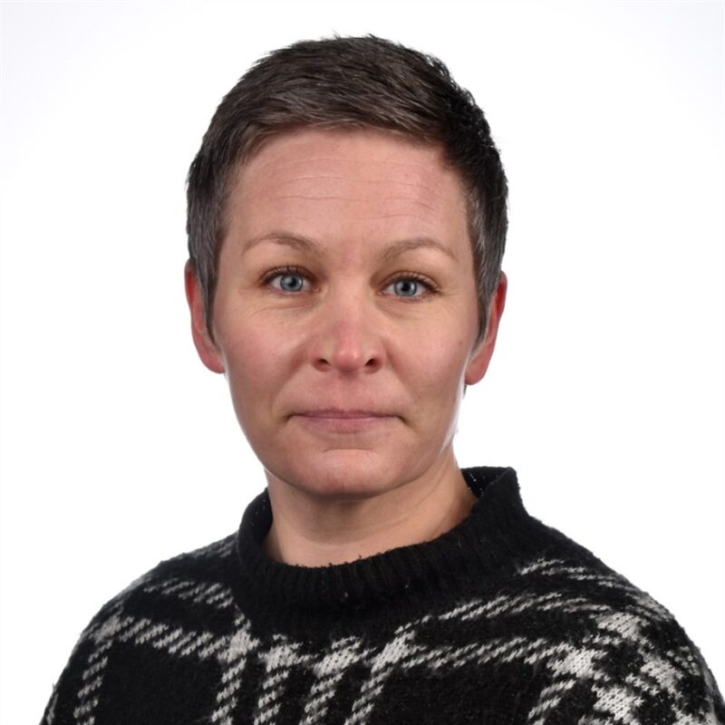 Lyhyttukkaisella henkilöllä on yllään mustavalkokuvioinen neule. He katsovat suoraan kameraan neutraalilla ilmeellä. Tausta on tavallinen valkoinen.