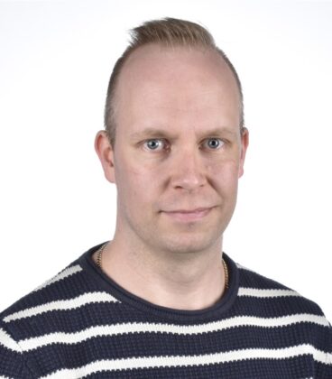 Henkilöllä, jolla on lyhyet, vaaleat hiukset, on yllään mustavalkoinen raidallinen pusero. He katsovat suoraan kameraan neutraalilla ilmeellä. Tausta on tavallinen valkoinen.