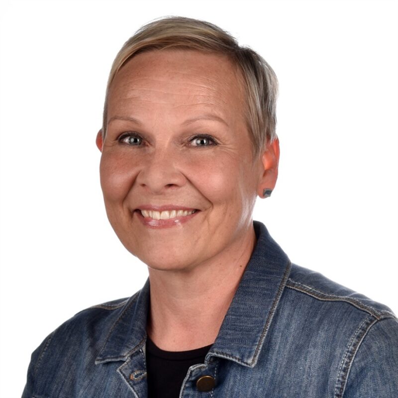 Lyhyet, vaaleat hiukset omaava henkilö hymyilee kameralle. Heillä on yllään farkkutakki ja musta paita. Tausta on valkoinen.