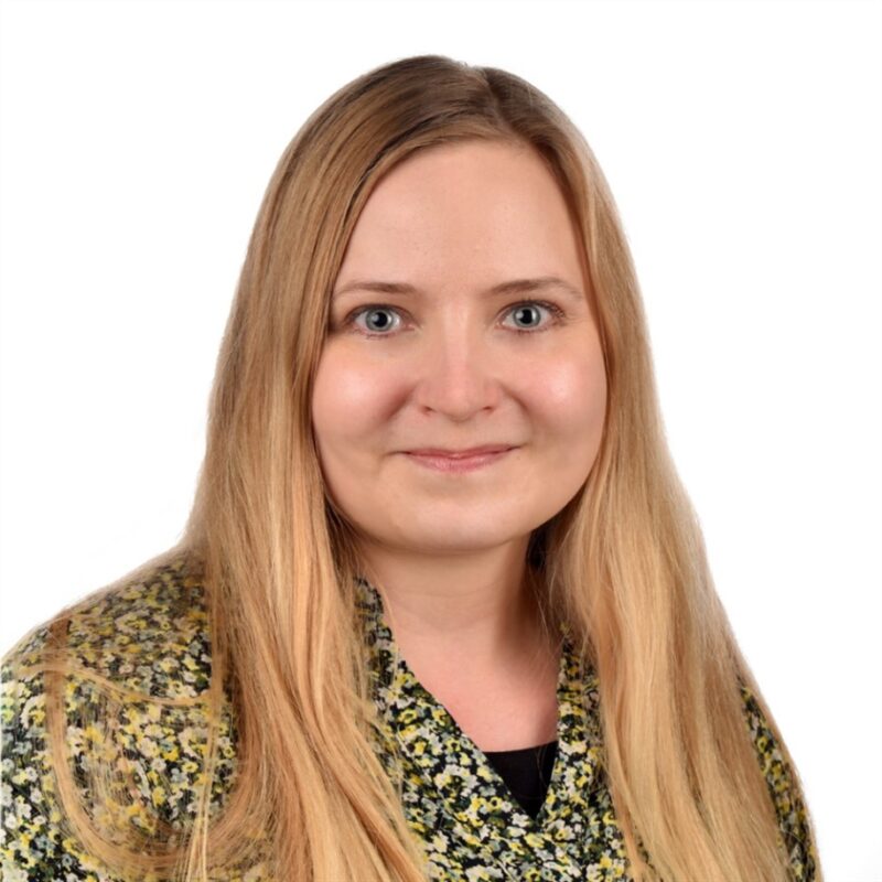 Pitkät vaaleat hiukset ja kuviollinen yläosa hymyilee kameralle valkoista taustaa vasten.